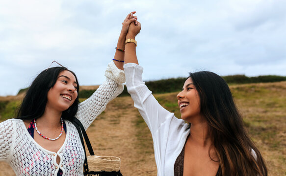 Joyful female friends raising arms in celebration outdoors