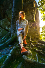 Smiling woman relaxing on mossy tree roots in sunlit mountain canyon, enjoying nature