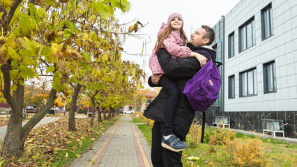 kid child with school backpack runs along road his father. father spins child girl daughter arms.