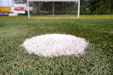 Konzept Strafstoß und Elfmeter beim Fußball: Nahaufnahme vom Elfmeterpunkt auf einem Kunstrasenplatz mit dem Tor im verschwommenen Hintergrund, viel Copy Space © redaktion93