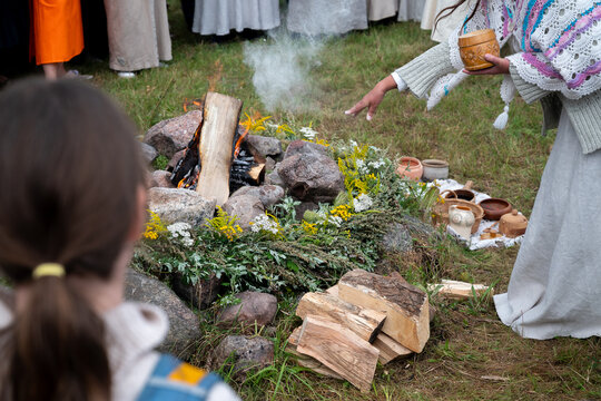 women wearing traditional slavic dresses stand in a circle around a campfire while a witch throws ashes into the bonfire casting spells