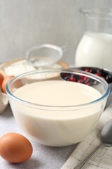 Liquid dough in bowl, berries and ingredients on light grey table, closeup