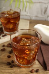 Tasty coffee with ice in glasses and beans on wooden table, closeup