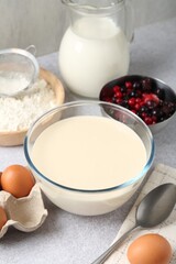 Liquid dough in bowl, berries and ingredients on light grey table, closeup