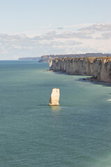 Lone white limestone rock formation rising from turquoise sea near Étretat, Normandy. Peaceful coastal scene showcasing the beauty of erosion and marine nature.