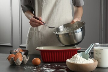 Woman with bowl of liquid dough at grey table in kitchen, closeup