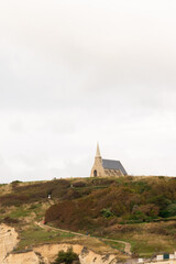 Small chapel on the cliff at Étretat, Normandy, France, surrounded by green hills and cloudy sky. Peaceful coastal landscape with natural and architectural harmony.