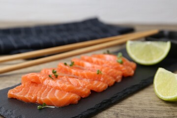 Fresh salmon sashimi with microgreens and lime on wooden table against grey background, closeup