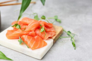 Fresh salmon sashimi with microgreens on grey textured table, closeup