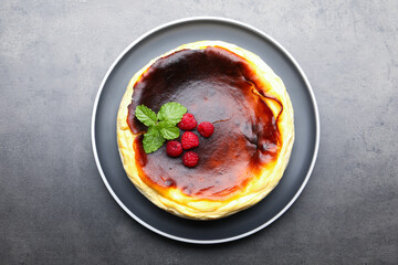 Tasty Basque cheesecake with raspberries and mint on grey textured table, top view