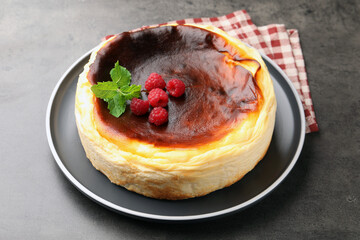 Tasty Basque cheesecake with raspberries and mint on grey textured table, closeup