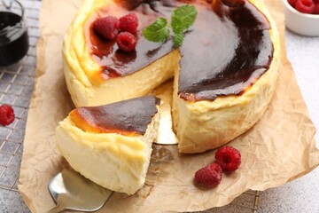 Tasty Basque cheesecake with raspberries and mint on light grey textured table, closeup