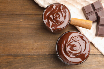 Melted chocolate and pieces on wooden table, flat lay. Space for text