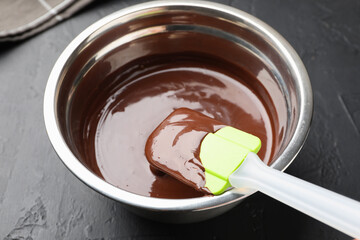 Melted chocolate and spatula in bowl on black table, closeup