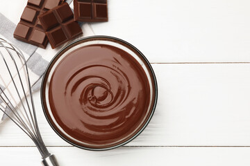 Melted chocolate, whisk and pieces white on wooden table, flat lay. Space for text