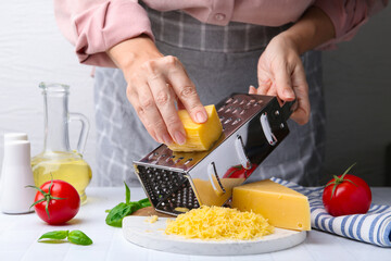 Woman grating cheese at white tiled table, closeup