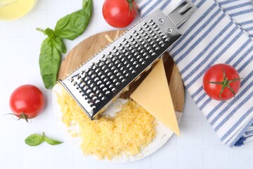 Grated cheese, grater and products on white tiled table, flat lay