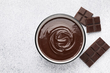 Melted chocolate in bowl and pieces on light grey table, flat lay. Space for text
