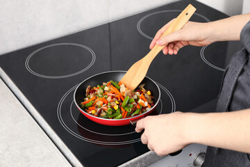 Woman stirring mix of fresh vegetables with wooden spatula in frying pan, closeup
