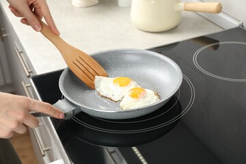 Woman taking fried eggs with slotted spatula in kitchen, closeup