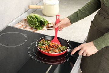 Woman stirring mix of fresh vegetables with slotted spatula in frying pan, closeup