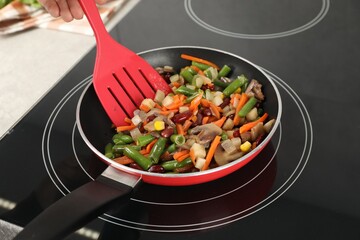 Woman stirring mix of fresh vegetables with slotted spatula in frying pan, closeup