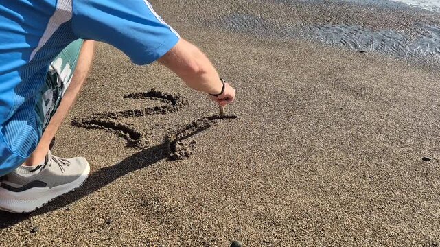 Beach sand drawing, person writing numbers, sunny day leisure activity by the water