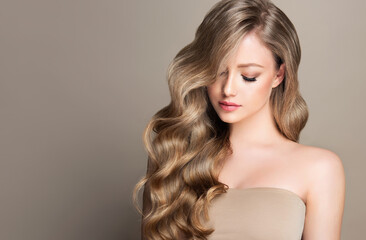 Blonde girl with long and shiny wavy hair . Beautiful model woman with curly hairstyle . Beauty and...