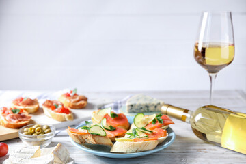 Tasty bruschettas with salmon, cucumber, lemon, olives and wine on light wooden table, closeup
