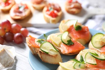 Tasty bruschettas with salmon, cucumber, lemon and cheese on light wooden table, closeup