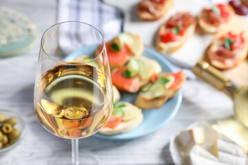 Glass of white wine and tasty bruschettas on white wooden table, selective focus