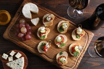 Tasty bruschettas with cheese, cucumber, sausages, honey and red wine on wooden table, flat lay