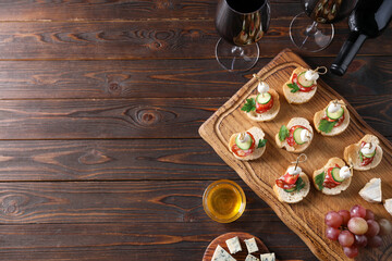 Tasty bruschettas with cheese, cucumber, sausages, honey and red wine on wooden table, flat lay. Space for text