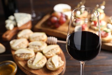 Glass of red wine and tasty bruschettas on wooden table, selective focus