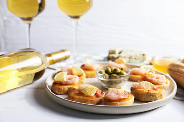 Tasty bruschettas with shrimps, lemon, olives and white wine on light wooden table, closeup
