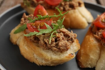 Delicious bruschettas with tuna, tomatoes and arugula on plate, closeup
