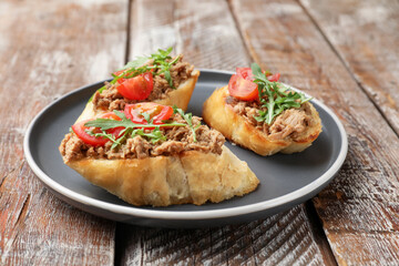Delicious bruschettas with tuna, tomatoes and arugula on wooden table, closeup