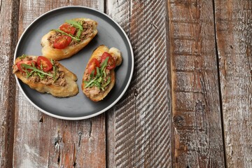Delicious bruschettas with tuna, tomatoes and arugula on wooden table, top view. Space for text