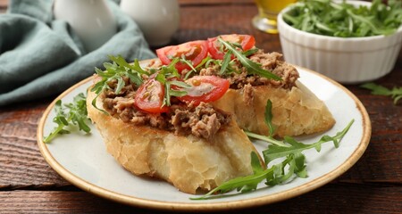 Delicious bruschettas with tuna, tomatoes and arugula on wooden table, closeup