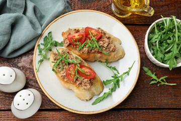Delicious bruschettas with tuna, tomatoes and arugula served on wooden table, flat lay