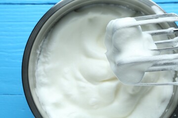 Whipped egg whites in bowl and mixer on blue wooden table, closeup