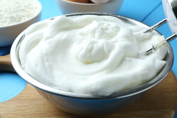 Whipped egg whites in bowl and mixer on blue wooden table, closeup