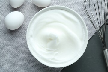 Fototapeta premium Whipped whites in bowl, whisk and eggs on grey wooden table, flat lay