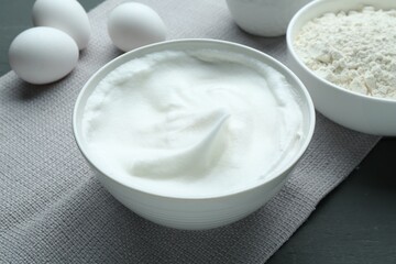 Whipped whites in bowl, flour and eggs on grey wooden table, closeup
