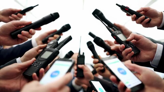 Close-up video of professional hands in suit sleeves holding microphones and smartphones, straining forward. Shallow depth of field with blurred bokeh background and soft lighting. Urgent demand for