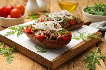 Delicious bruschettas with tuna, tomatoes, onion and arugula on wooden table, closeup