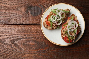 Delicious bruschettas with tuna, tomatoes, onion and arugula on wooden table, top view. Space for text