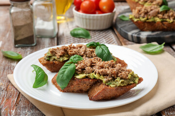 Delicious bruschettas with tuna, avocado and basil on wooden table, closeup