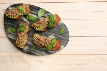 Delicious bruschettas with tuna, avocado and basil on light wooden table, top view. Space for text