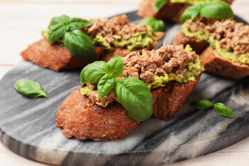 Delicious bruschettas with tuna, avocado and basil on light table, closeup